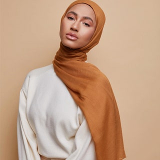 Voile Chic Breathable Modal model looking into the camera wearing burnt orange hijab on tan background